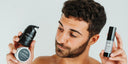 Hyaluronic acid for men: bearded man looking at the FETĒN face moisturiser and face scrub in his right hand, holding the hyaluronic acid serum in his left