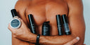 Kit soin visage homme : homme aux bras croisés tenant le gommage, la BB Crème, les sérums, le contour des yeux et la crème visage FETĒN